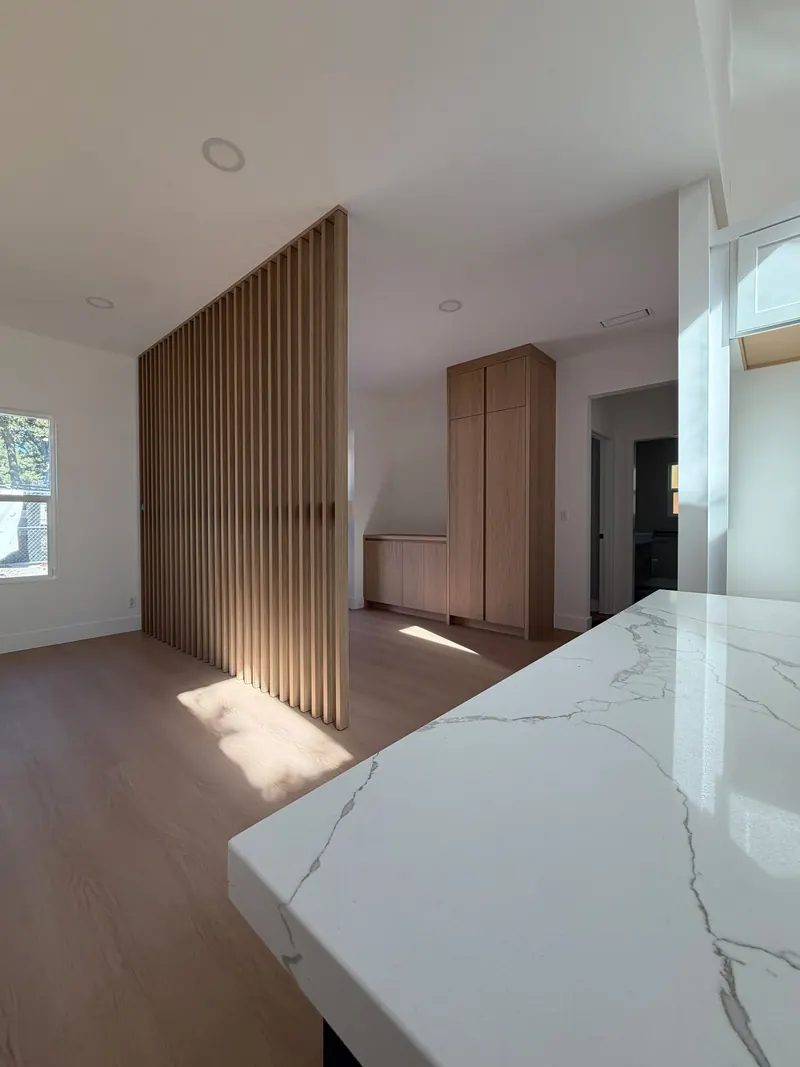 Open living area with a floor-to-ceiling wood slat divider, built-in cabinetry and a white quartz counter