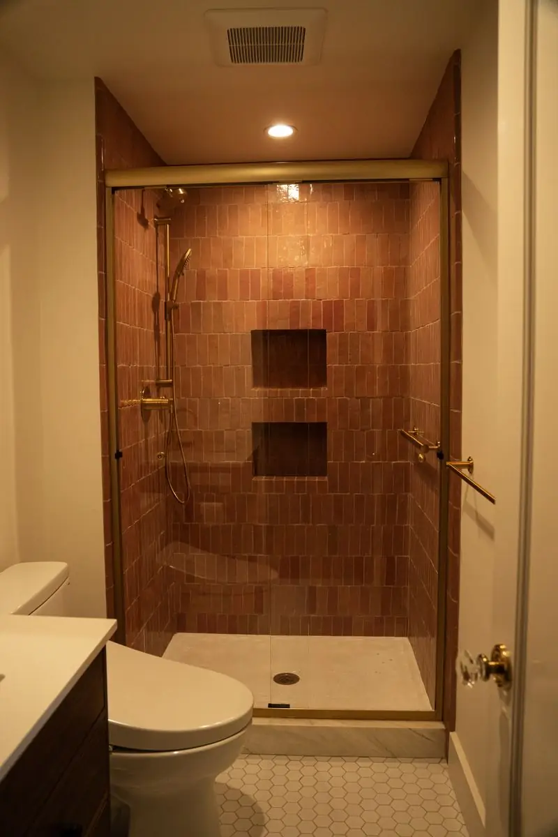 Bathroom with green zellige tile, brass shower fixtures and glass enclosure